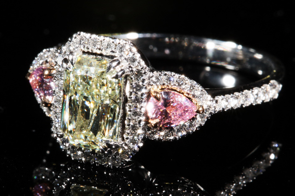 A radiant cut stone of soft chartreuse between two pear shaped pink companions, carried on a pavé band.