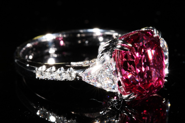 A cushion cut stone of vivid crimson between trillion cut diamonds