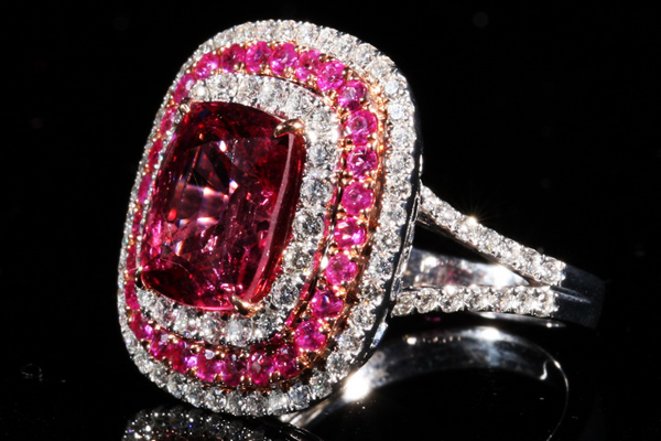 A cushion cut stone of deep rose within a double surround of pink gems and diamonds.