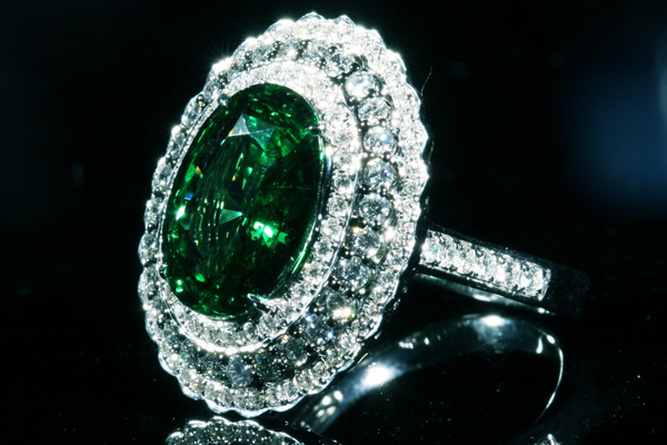 An oval gem of deep forest green in a double diamond halo
