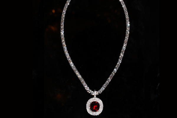 An oval gem of saturated red within a diamond surround, on a rivière of brilliant cut diamonds.