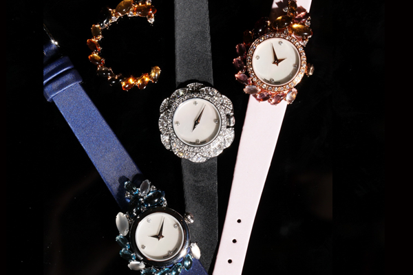 Three jewelled timepieces, each garden of gems in a different colour, on satin.
