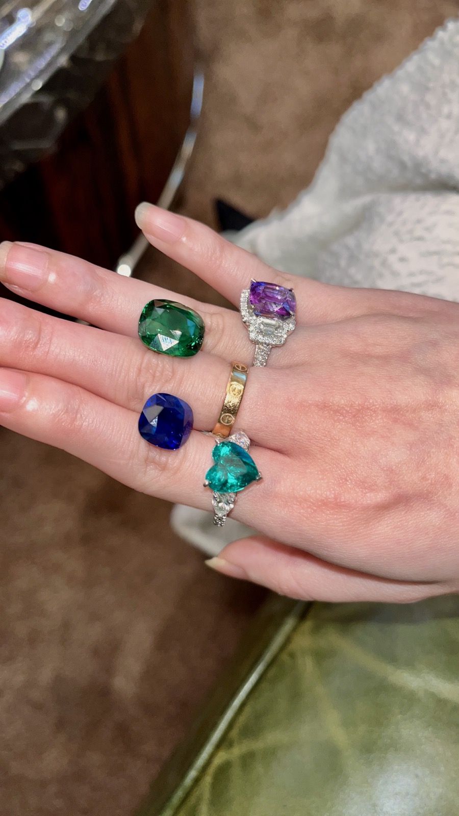 A hand carrying loose coloured gemstones alongside gem set rings at a private viewing